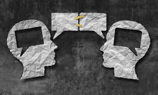 Speaking together media concept as two crumpled pieces of paper shaped as a human head with talk bubbles or speech bubble icons taped as a communication symbol for business understanding and compromise agreement.