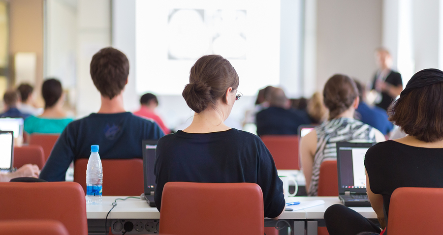 Workshop at university. Rear view of students sitting and listening in lecture hall doing practical tasks on their laptops. ** Note: Shallow depth of field